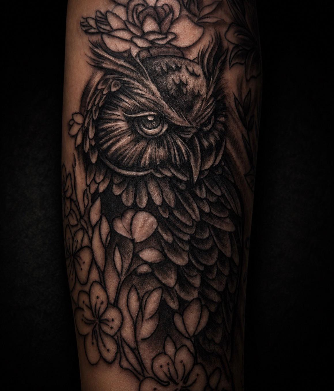 Realistisches Black-&-Grey-Tattoo einer Eule mit Blüten am Unterarm